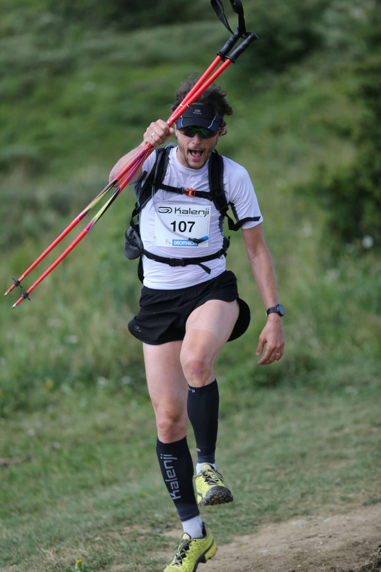 Corredor caminhando na subida de trail running em trilha íngreme com bastões nas mãos
