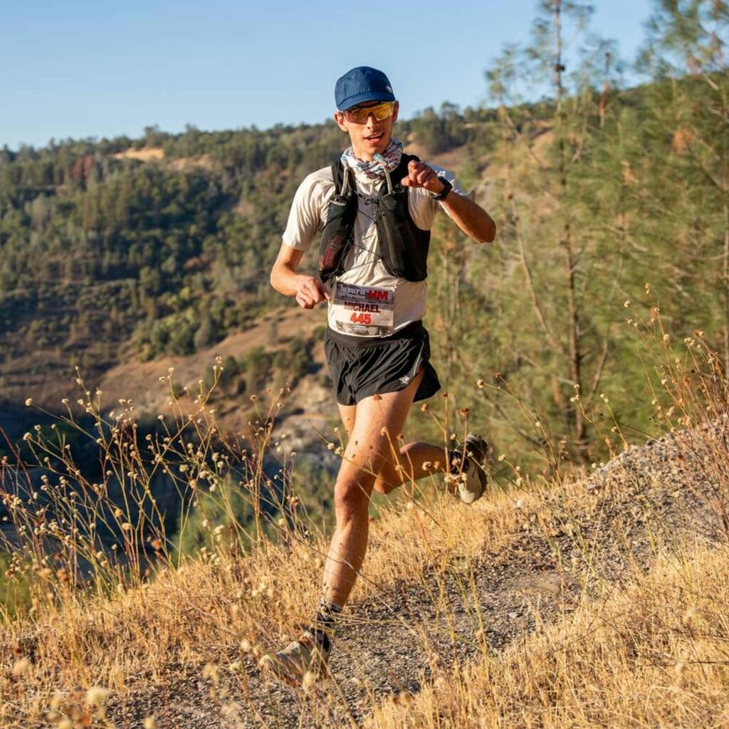 Corredor usando colete de hidratação para trail running em trilha de montanha com garrafas frontais visíveis