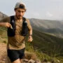 Gel de carboidrato ou hidrogel: qual usar na corrida? 5 Gel de carboidrato para corrida: trail runner acessando sachê no colete durante prova com nutrição esportiva e hidratação