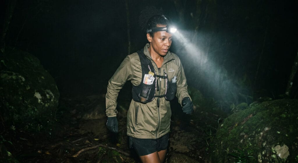 Lanterna para ultra trail noturna: corredora com headlamp em trilha de Mata Atlântica durante a noite de prova