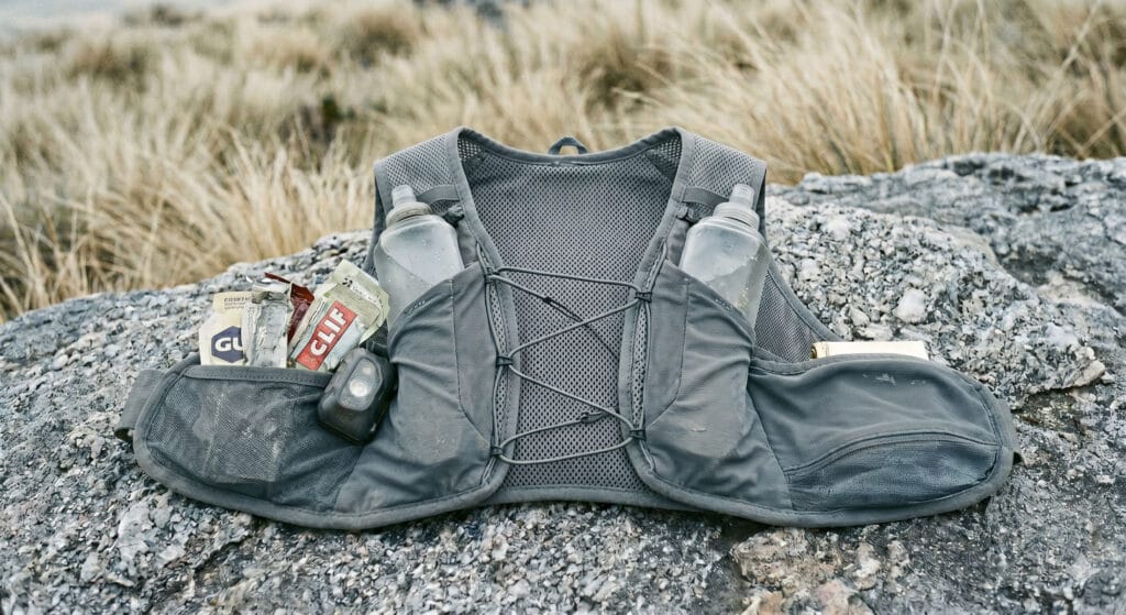 Mochila para ultra trail de inverno: colete organizado com soft flasks, lanterna e manta térmica em campos de altitude